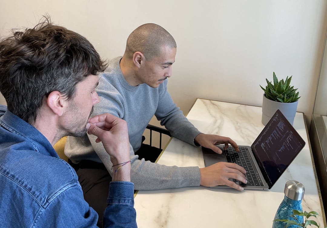 Picture of Mehdi and Nicolas looking at code on a laptop screen in an office